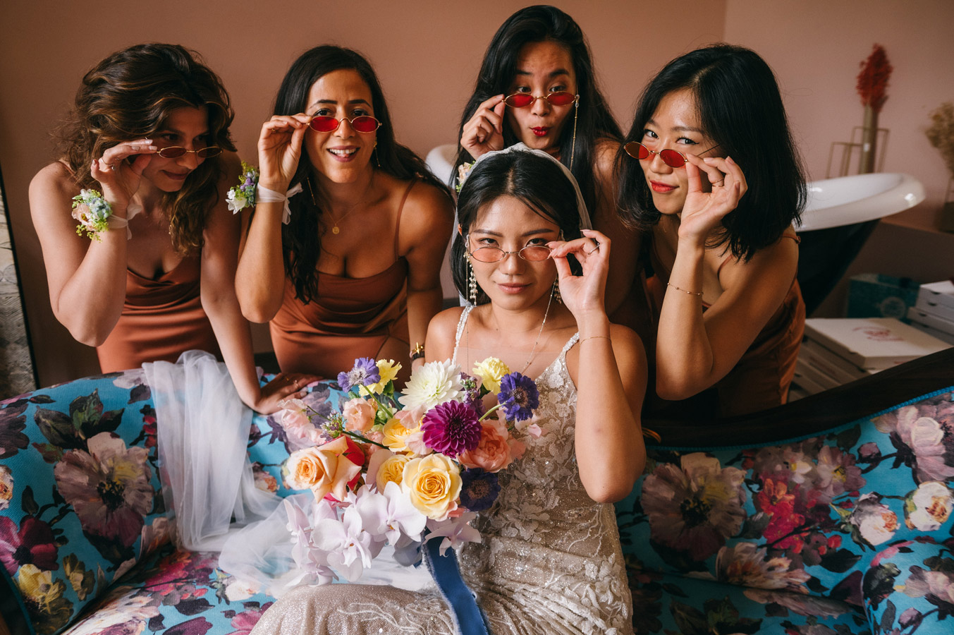 Mariée entourée de ses demoiselles d’honneur portant des lunettes rouges pendant les préparatifs du mariage