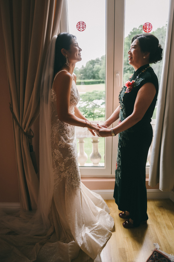 Mariée tenant les mains de sa mère devant une fenêtre pendant les préparatifs du mariage