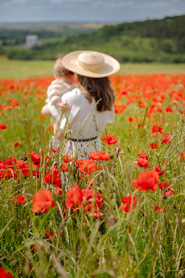 Mère portant son bébé dans un champ de coquelicots lors d’une séance photo famille en extérieur en Bourgogne