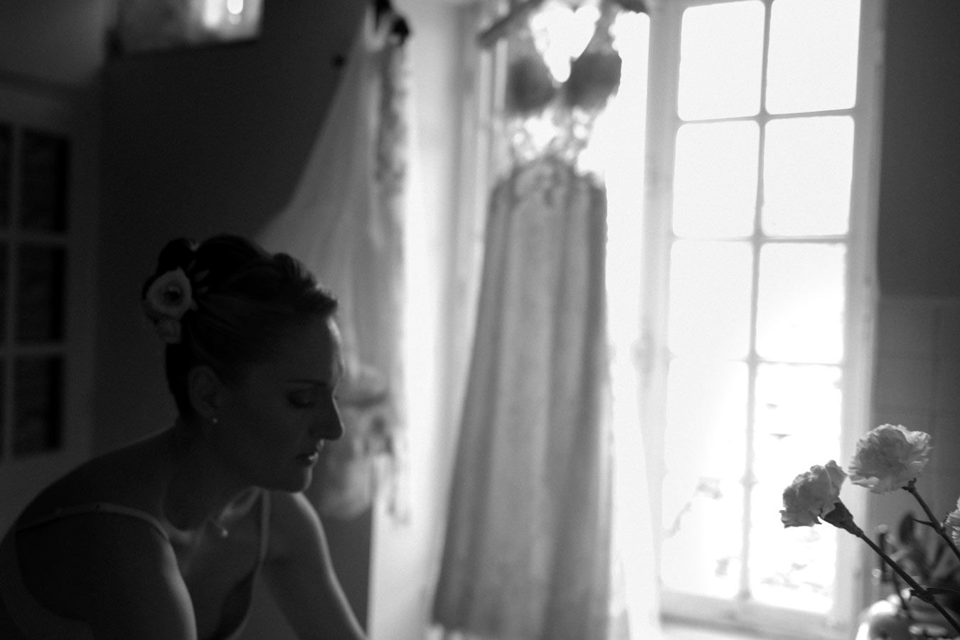 Mariée se préparant près d’une fenêtre avec sa robe suspendue pendant les préparatifs du mariage