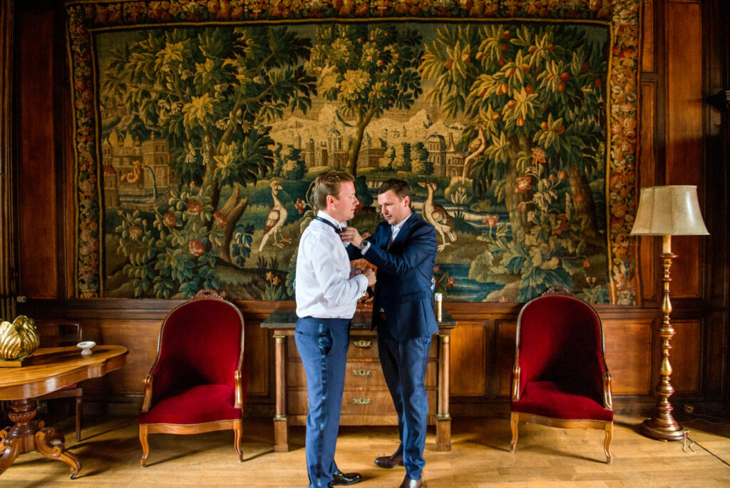 Le témoin aide le marié à ajuster son nœud papillon pendant les préparatifs du mariage au château de Chevillon en Bourgogne